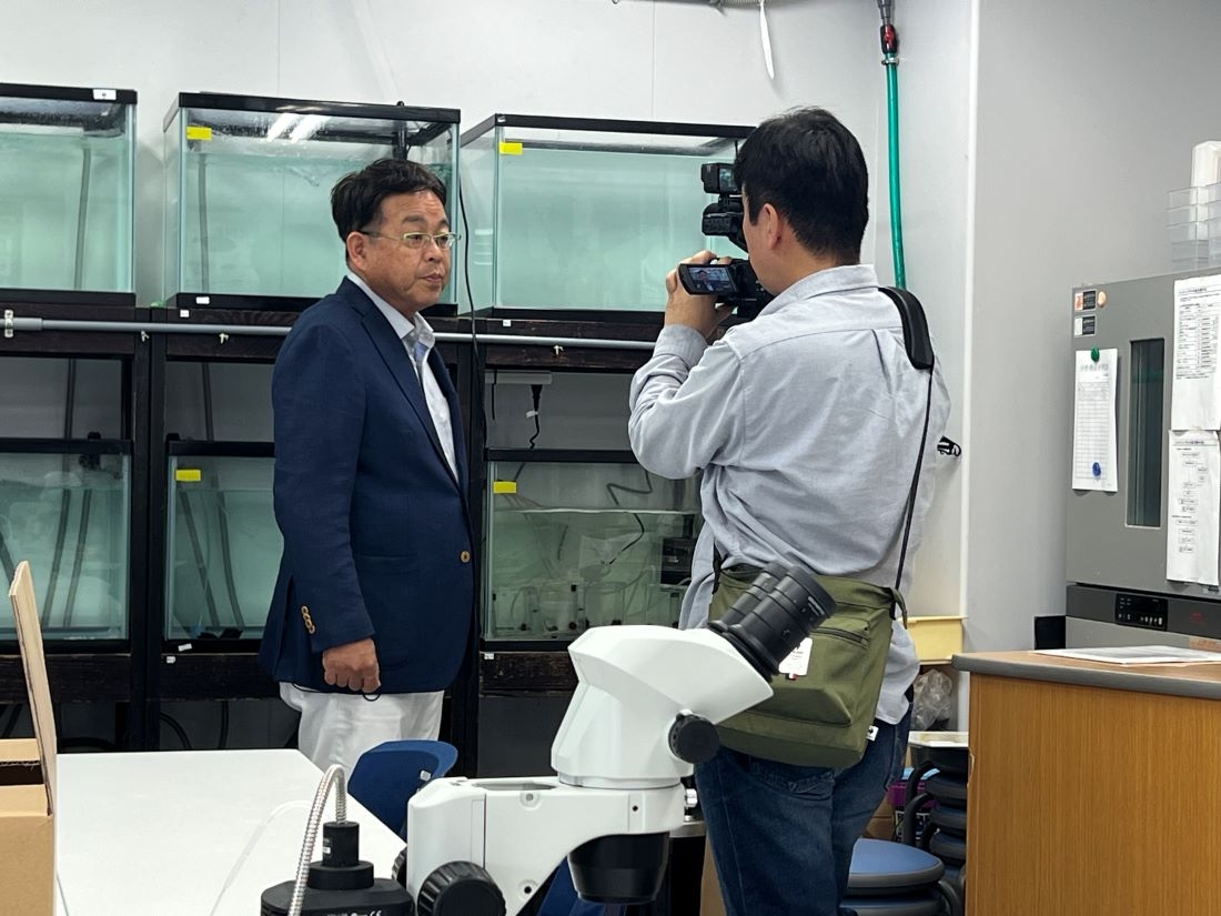 テレビ局の取材を受ける山本准教授(左)