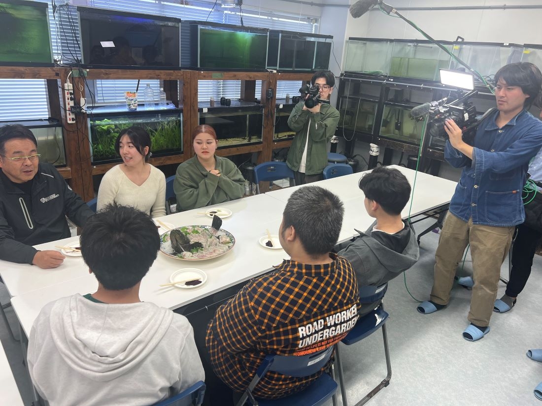学生たちと一緒にタマカイを試食しながら取材を受ける山本准教授(左端)