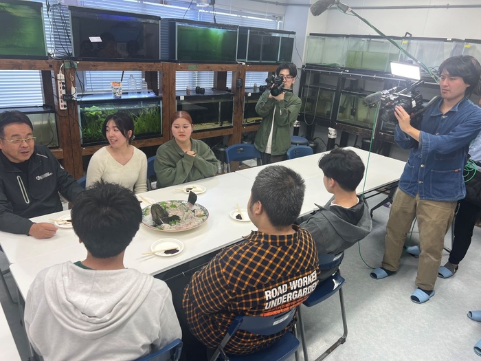 学生たちと一緒にタマカイを試食しながら取材を受ける山本准教授(左端)