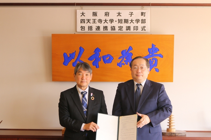 太子町の田中 祐二町長(左)と、須原 祥二学長(右) = 12月15日(木)、背景の「以和為貴」は17条憲法の第1条「和を以て貴しとなす」