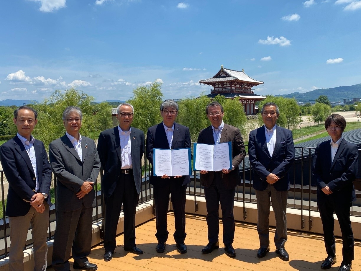 写真左から、近畿大学農学部准教授 大石 卓史、近畿大学リエゾンセンター長 竹原 幸生、近畿大学副学長・農学部長 江口 充、近畿大学学長 細井 美彦、(株)ネクスト・アクシス代表取締役 大川 裕之、なら歴史芸術文化村 総括責任者 福原 稔浩、県営平城宮跡歴史公園 総括責任者 粟坂 史明