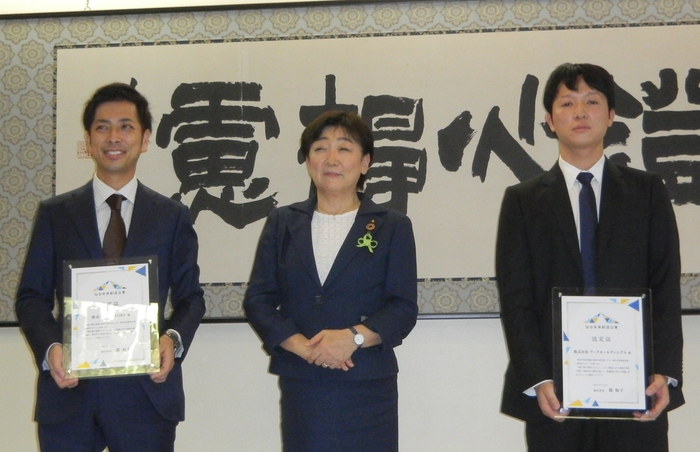 認定書を手に郡市長を挟んで並ぶ粕川社長(右)と歌川社長(左)