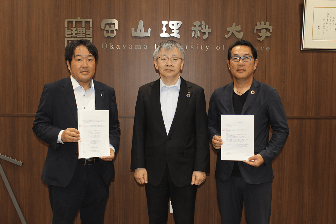 パートナーシップ契約を結んだ「(株)ウッディワールドのざき」の野﨑社長(左)と理大サッカー部の秦監督(右)。中央は平野学長