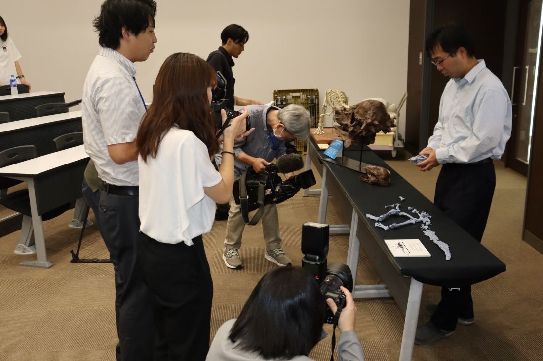 ザヴァケファレの実物大化石のレプリカを手に報道関係者に解説する高崎助教(右)