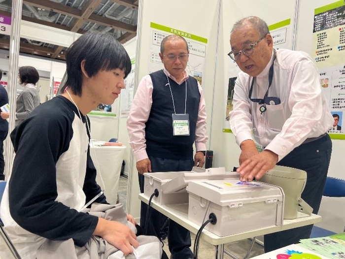 辻教授(右)の説明に聞き入る来場者の大学生。中央は轟代表取締役