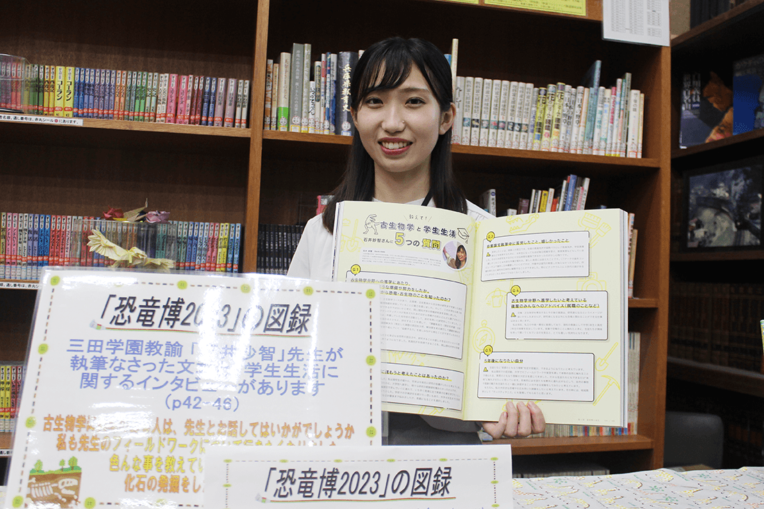 「恐竜博2023」の図録で、自分が紹介されているページを開く石井さん(三田学園中学・高校図書館で)