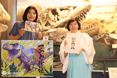 岡山理科大学恐竜学博物館のタルボサウルスの頭部標本の前で（左から）市川さんと久山さん。左下は恐竜御朱印