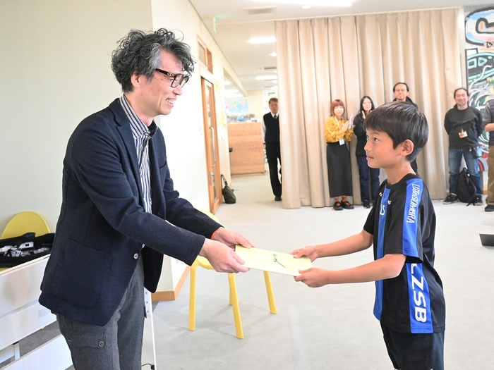 執行役員 山里尚和より生徒代表に目録贈呈