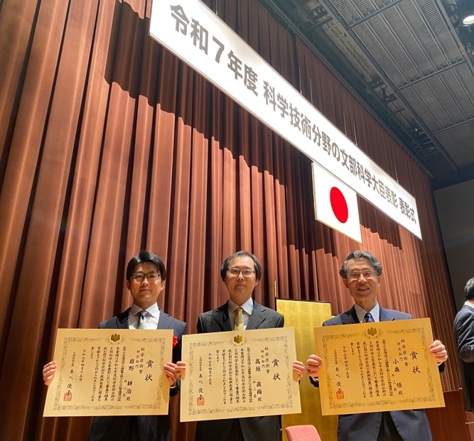 文部科学省で4月15日に行われた表彰式で、賞状を手に記念写真に納まる(左から)岩野准教授、高垣教授、小森名誉教授