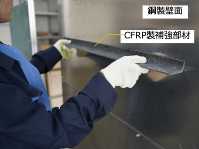 補強部材を壁面に接着している様子*（写真の試験体は本公開実験と異なります）