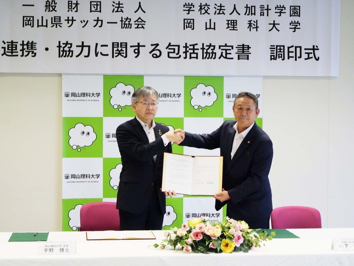 協定書に署名後、がっちり握手する山下会長(右)と平野学長(左)