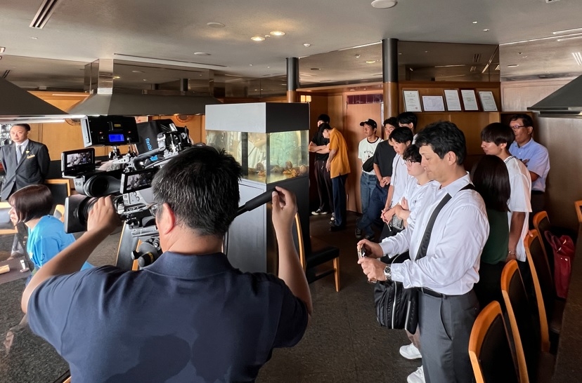 テレビの撮影風景を見学するラボの学生たち=ホテルグランヴィア岡山で