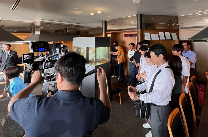 テレビの撮影風景を見学するラボの学生たち=ホテルグランヴィア岡山で