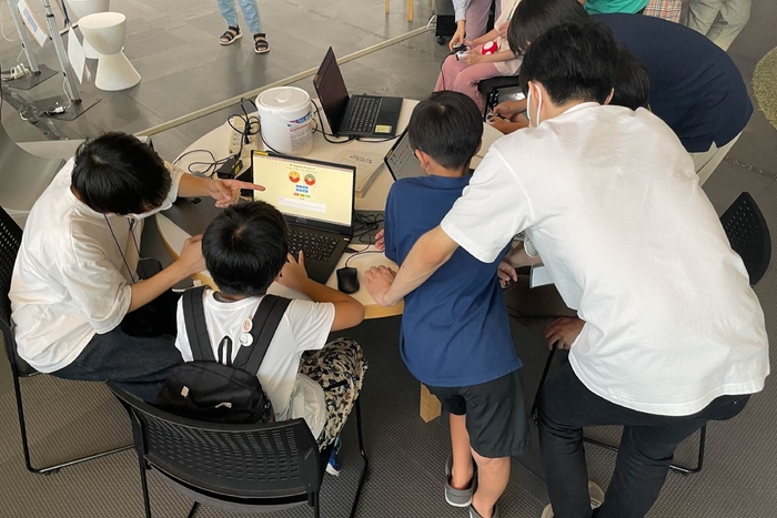 日本科学未来館のイベントでゲームを プレイする子供たちとサポートの大学院生
