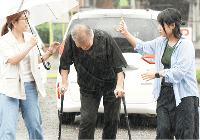 雨の中、杖を使って「いこい」へ。同行したリハビリ職員が傘を差しながら付き添いました。