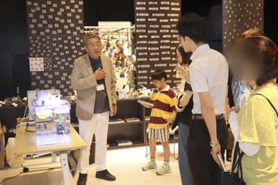 宇宙養殖実験水槽を前に参加者に実験内容を解説する山本准教授（左）