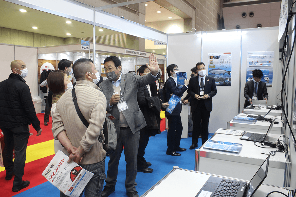 養殖の映像を前に来場者に案内する山本准教授(中央)