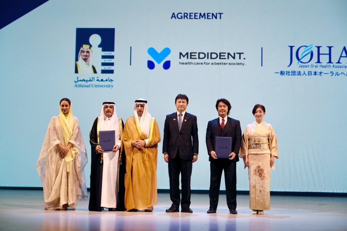 「大阪・関西万博『日・サウジEXPO投資フォーラム』壇上での調印。左から:アルファイサル大学・ヌール・A・アル・サアドゥーンセンター長、アルファイサル大学ムハンマド・Ali・アル・ハイアザ学長、サウジアラビア王国ハーリド・アル=ファーレフ投資大臣、古賀友一郎経済産業副大臣、メディデント代表 富田大介、一般社団法人日本オーラルヘルス協会富田由美子理事」