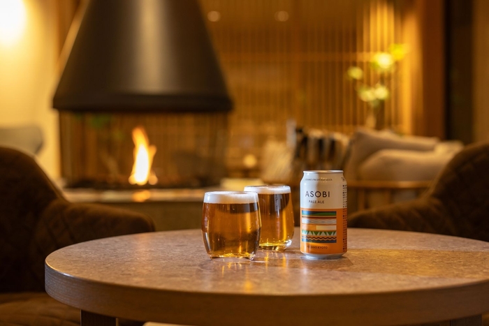 【ラウンジ】暖炉のやわらかな灯に包まれ、旅の疲れをそっとほぐしてくれるひととき。ゆらぐ光を眺めながら、クラフトビールとともにくつろぎの時間を──。