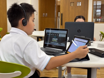 メタバースに参加するPCと、同時通訳機能を使うタブレットを操作する児童