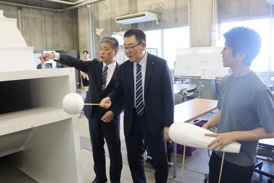 風洞実験装置を試してみる烏田社長（中央）ら。右は機械システム工学科の岩野耕司准教授