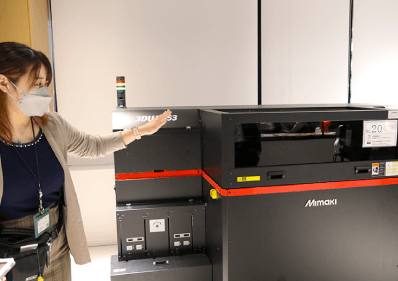 ビジネスサポートファクトリーの目玉となる装置、フルカラー３Dプリンタ 手ごろな料金で利用できると学生から社会人まで好評 説明するのは、㈱キャンパスクリエイト・クリエイティブコーディネーターの永井恵梨氏