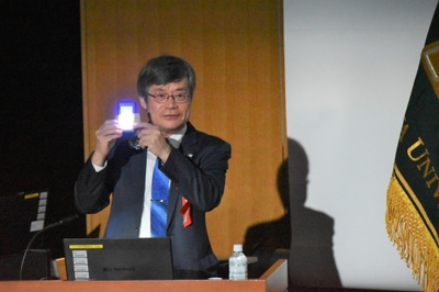 青色LEDで白色光を作る原理を見せながら説明する天野教授