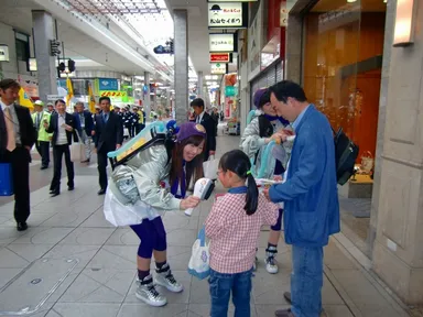 パレードで通行中の市民やドライバーにインペアード・パフォーマンスの注意呼びかけ