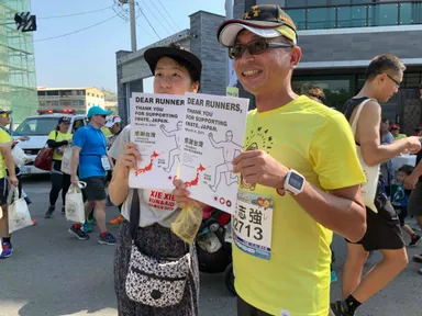 田中マラソン：ゴール地点でランナーに復興支援感謝を伝えるファイル配布しているシーン