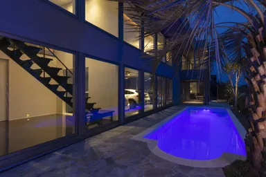 夕暮れ時の庭のプールサイドでは大きなココスヤシやソヨゴが潮風になびく