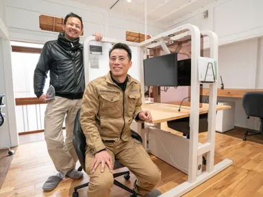 今回シンマチに導入した4人掛けの「KAKINE」と代表取締役の伊藤(左)とKAKINE開発者の松本