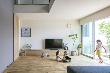 屋外のウッドデッキからフラットにつながる開放的なリビングで走り回る子どもたち
