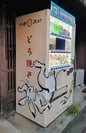 店舗玄関横に鎮座する鳥獣戯画の自動販売機、上中下段3段の1番下の段がどら焼き販売スペース