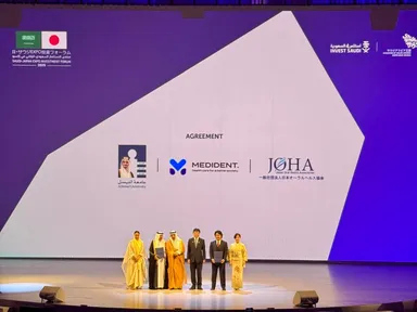 会場スクリーンに表示された提携3者のロゴ(Alfaisal University／MEDiDENT／日本オーラルヘルス協会)。公式プログラムとして壇上で合意。