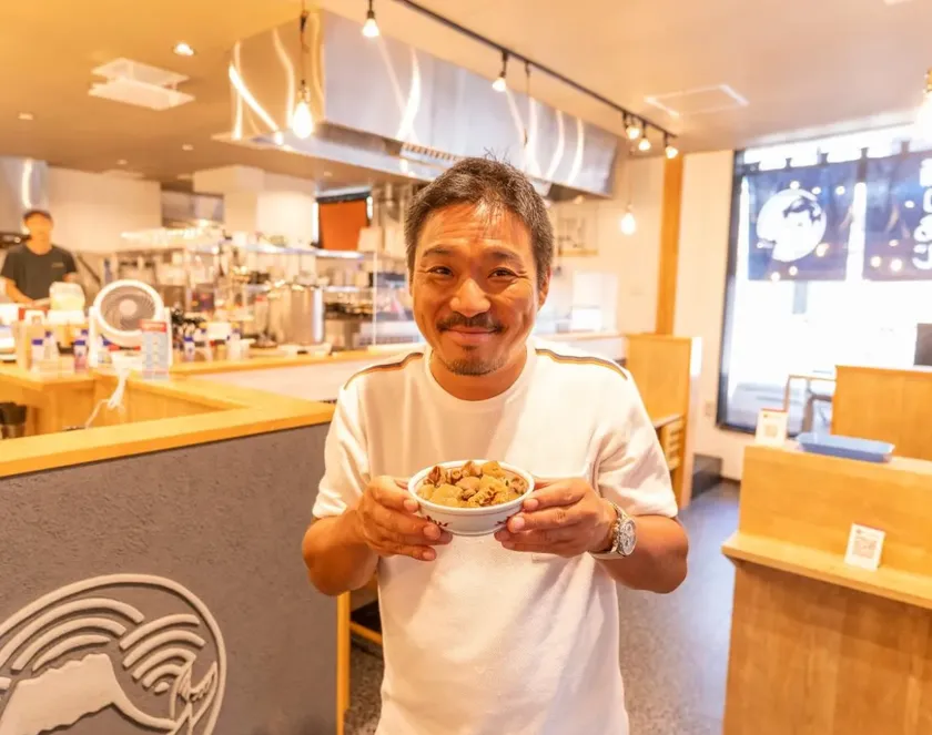 「大衆酒場 たばちゃん 仲見世店」の人気商品「おやじのもつ煮込み」を持つ代表の望月