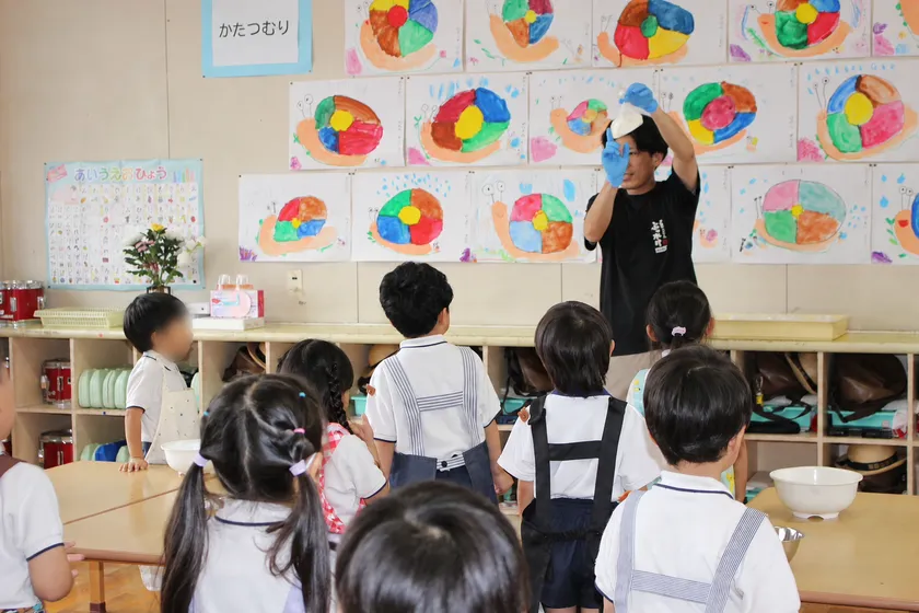 スタッフがうどん作りの工程を実演し、興味深そうに見学する園児たち